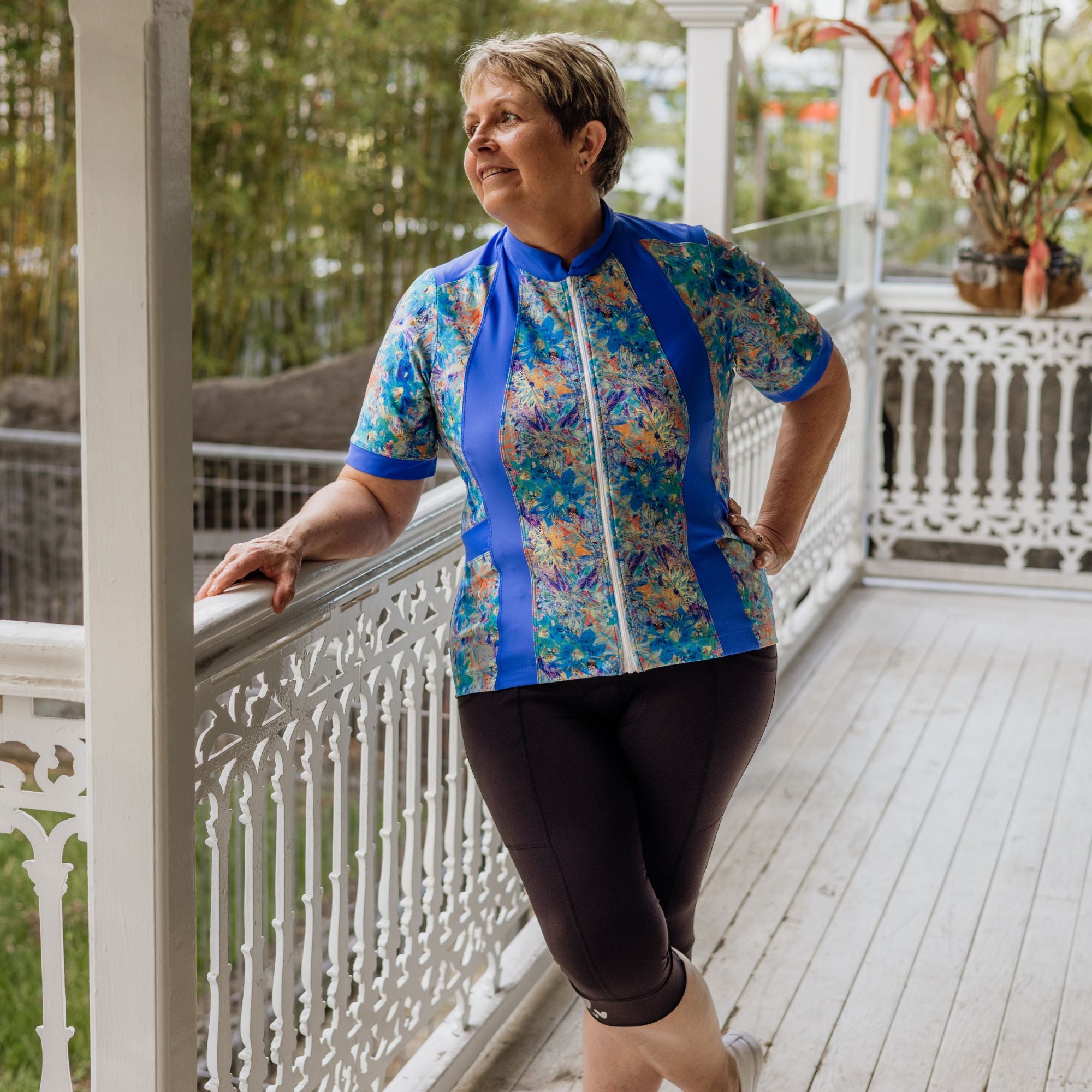 Cyclist leaning on a railing wearing blue artsy floral carefree cycling jersey and black knicks