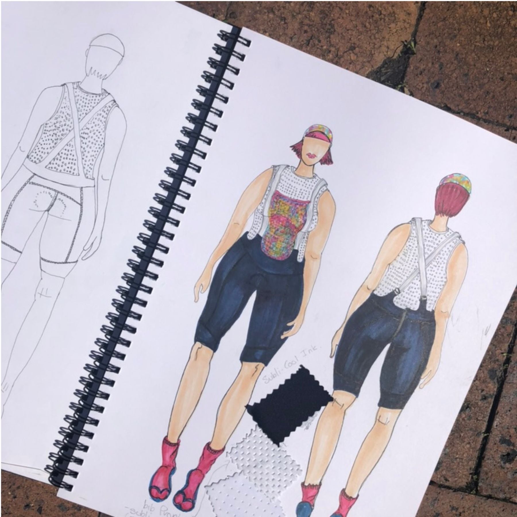 A spiral-bound sketchbook lying on a brick surface, showing fashion illustrations of a sleeveless patterned top and dark cropped shorts on a white page.