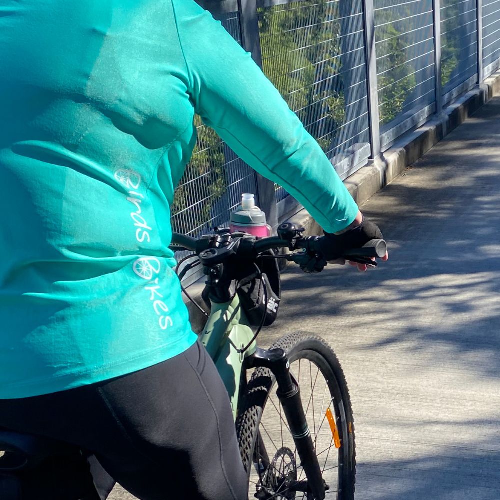 Woman cycling on a trail wearing Light Teal tee, added sleeve coverage