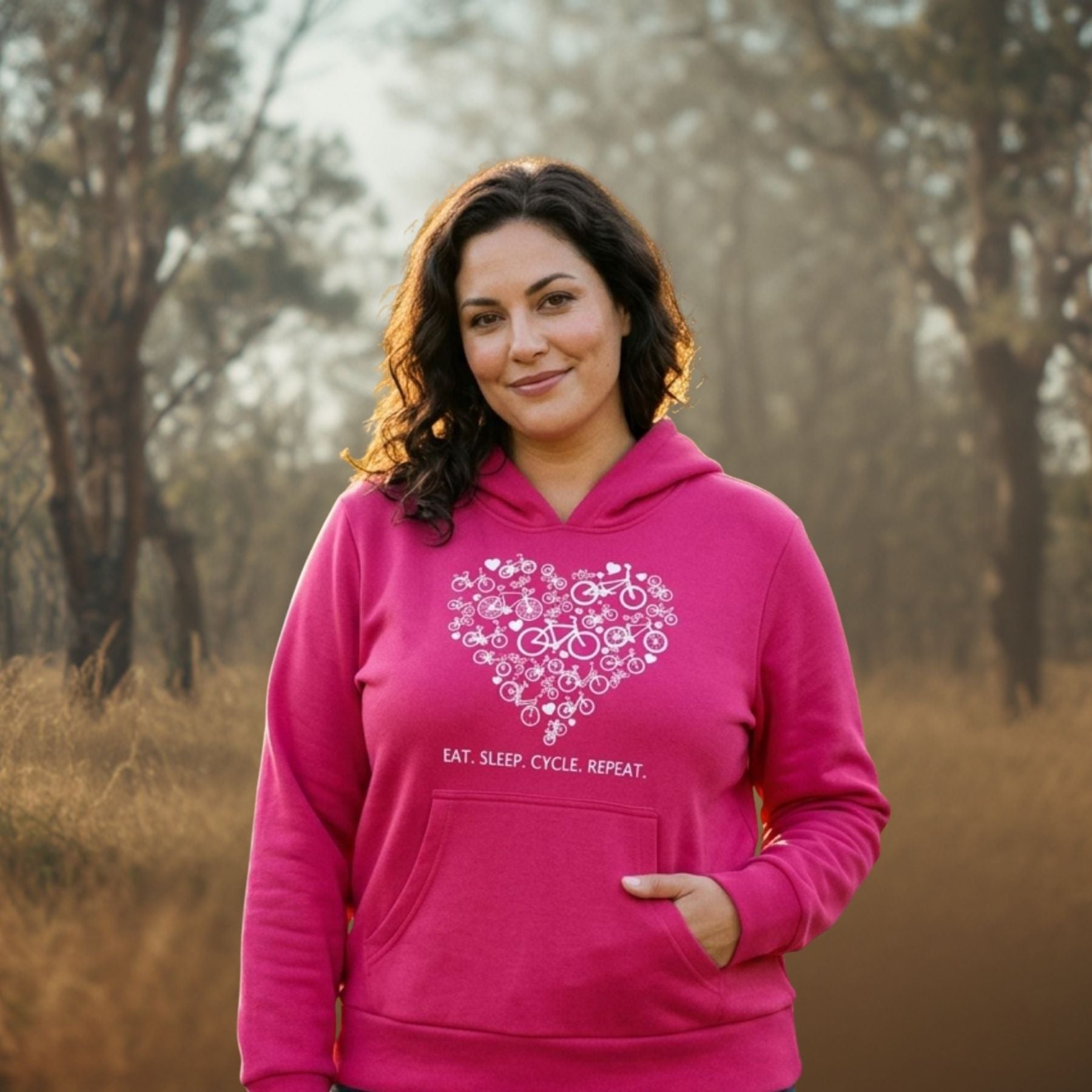 A woman wearing a bright pink hoodie with a white bicycle-heart graphic and the text 'EAT. SLEEP.