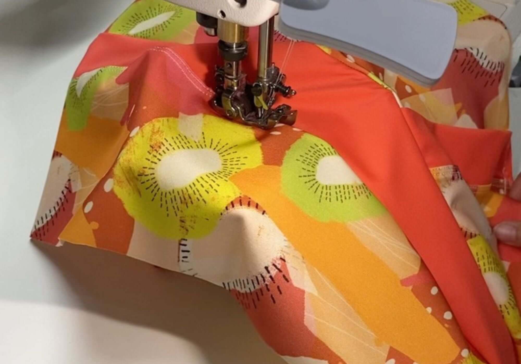 Sewing machine needle piercing through colorful fabric with a floral pattern.