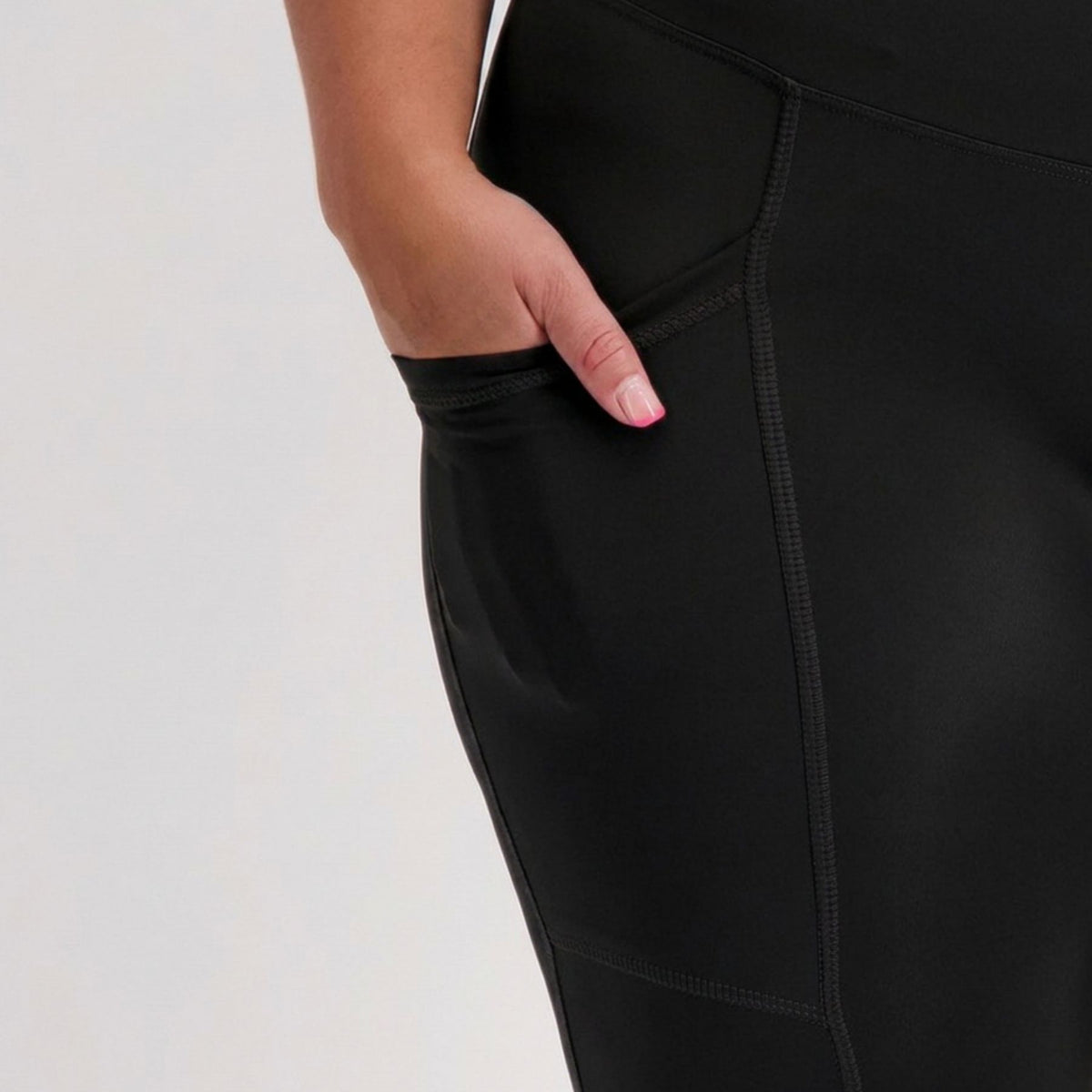 Close-up of a person wearing black padded cycling pants with a side pocket, showing the hand reaching into the pocket against a light gray background.