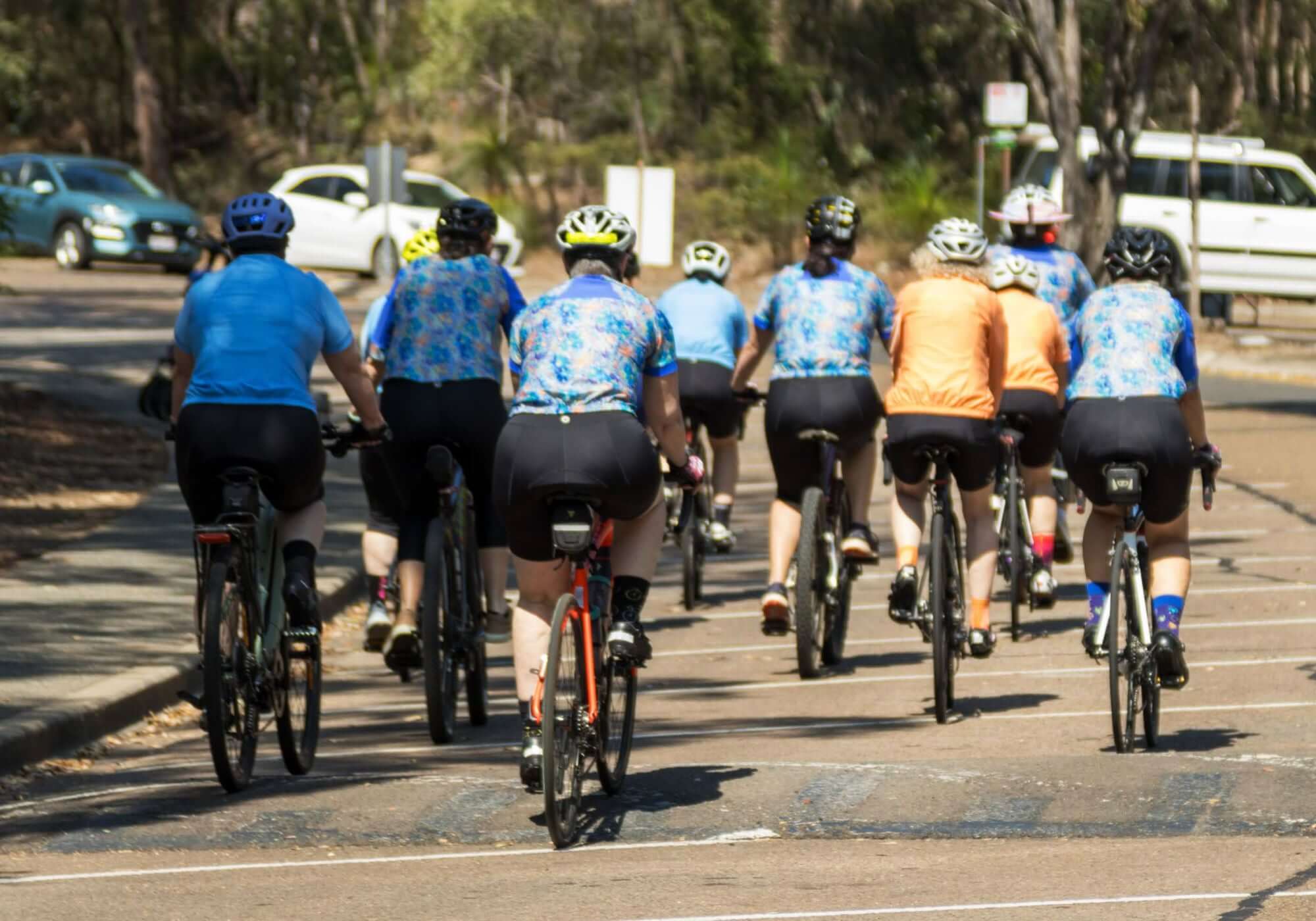 Group of cyclists riding on a road with trees and cars in the background