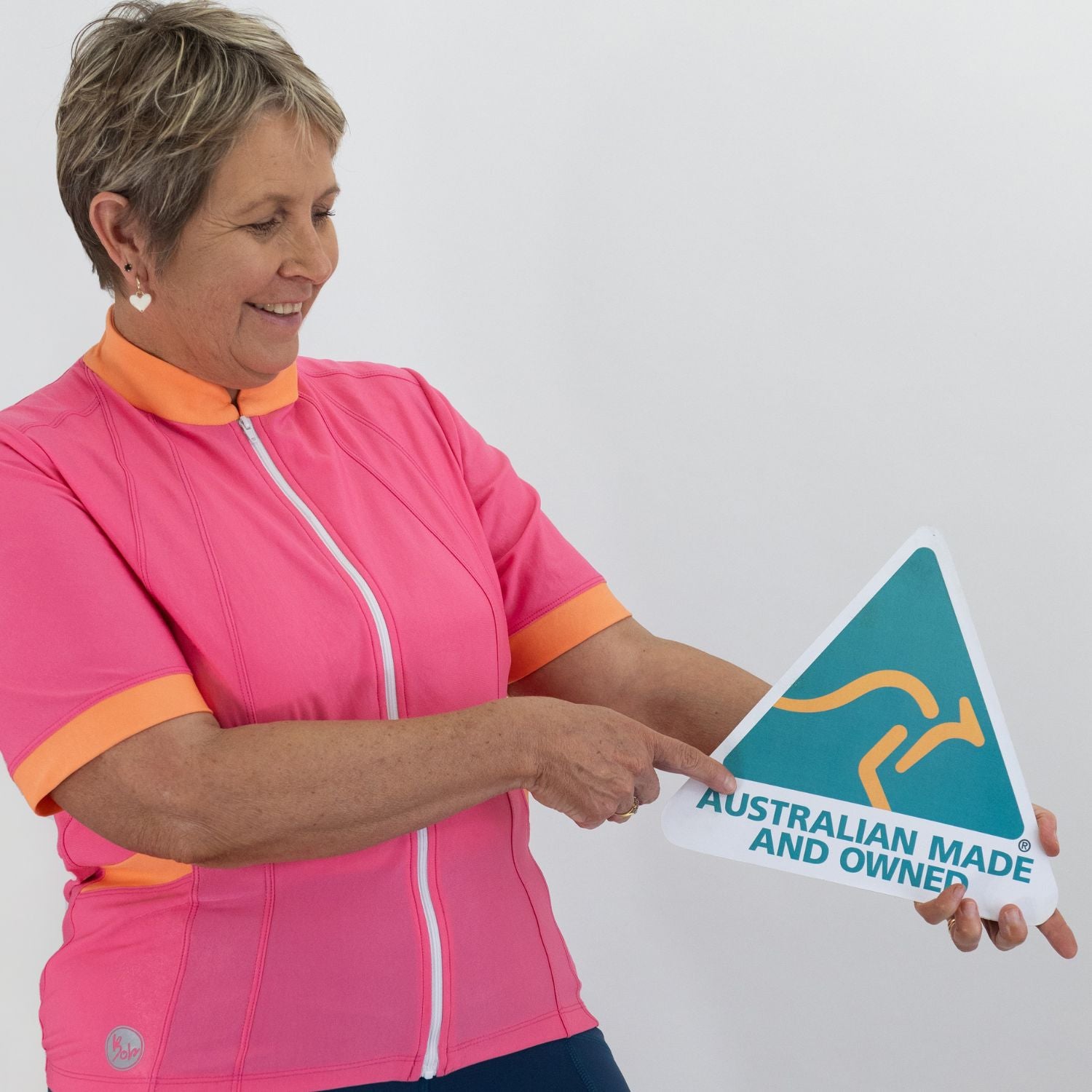 Woman in pink and orange cycling outfit holding an 'Australian Made and Owned' sign.