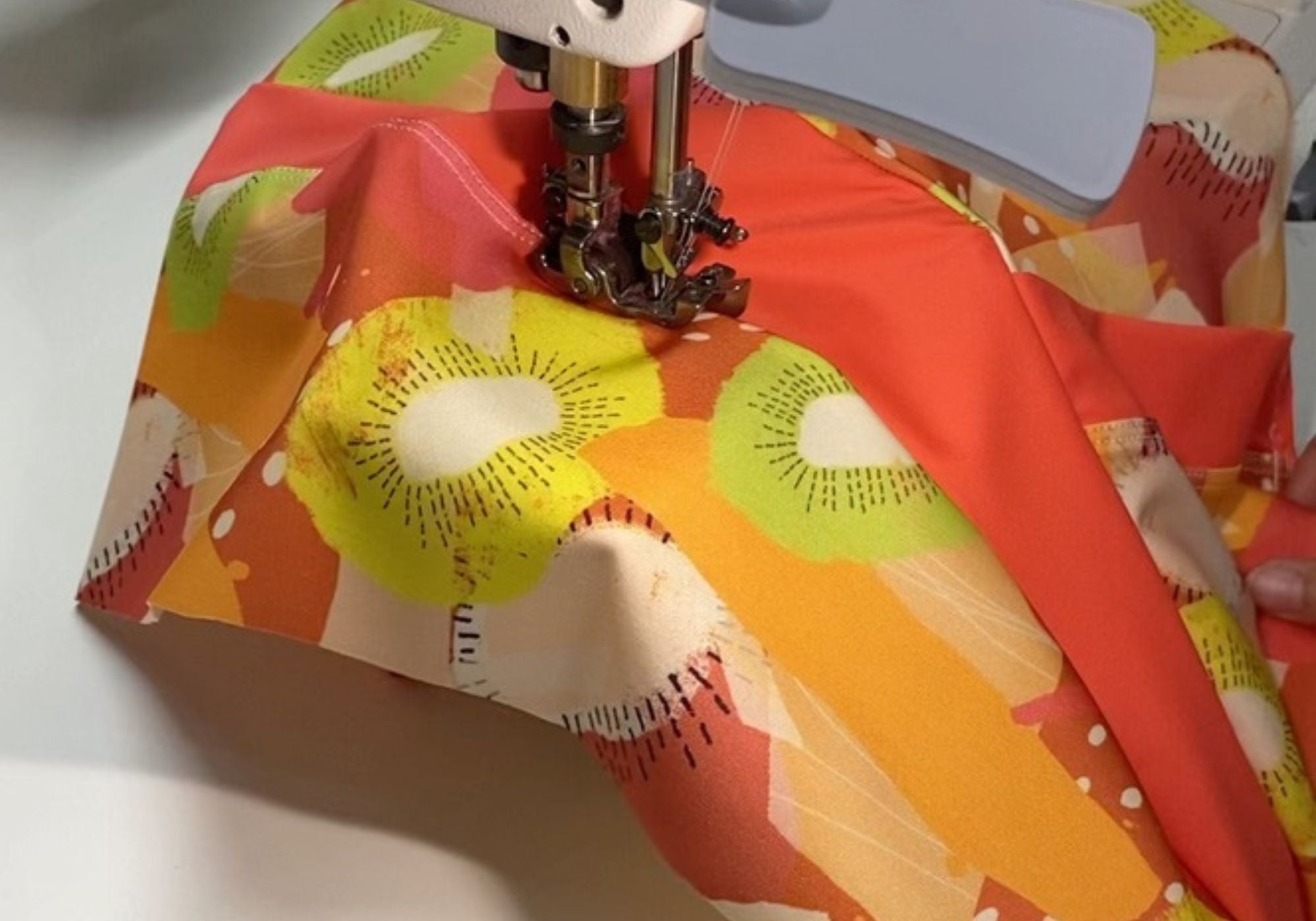 Sewing machine needle piercing through colorful fabric with a floral pattern.