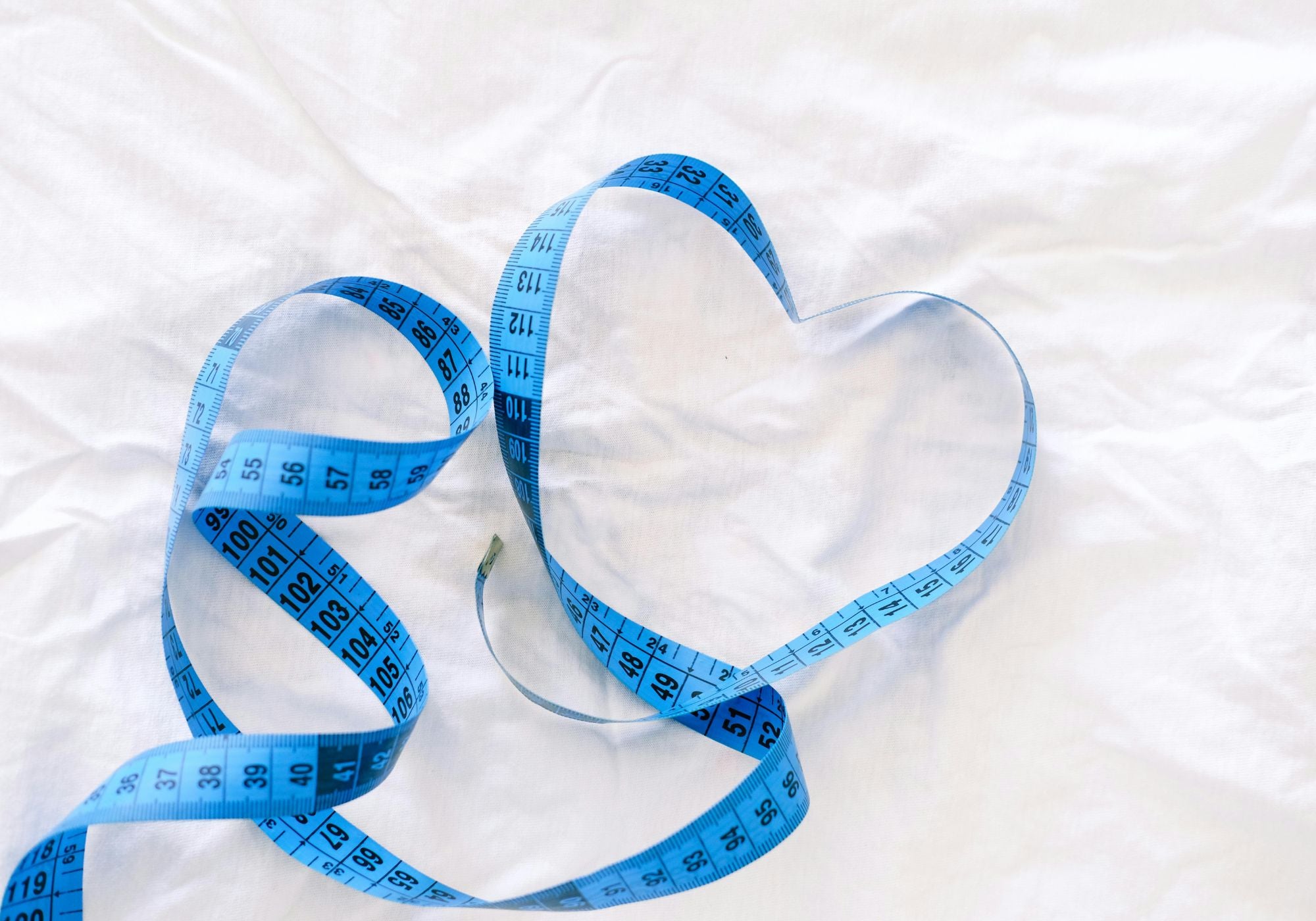 Blue measuring tape shaped into a heart on a white background