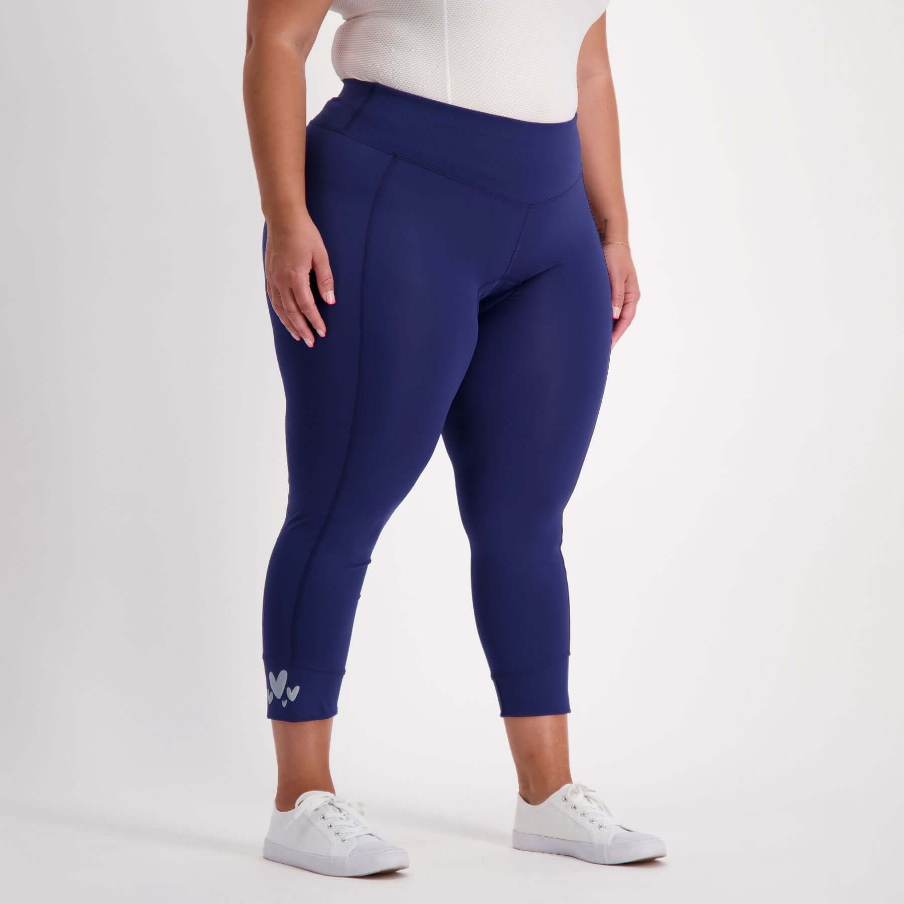 Person wearing blue padded bicycle capri leggings and white sneakers on a light gray background
